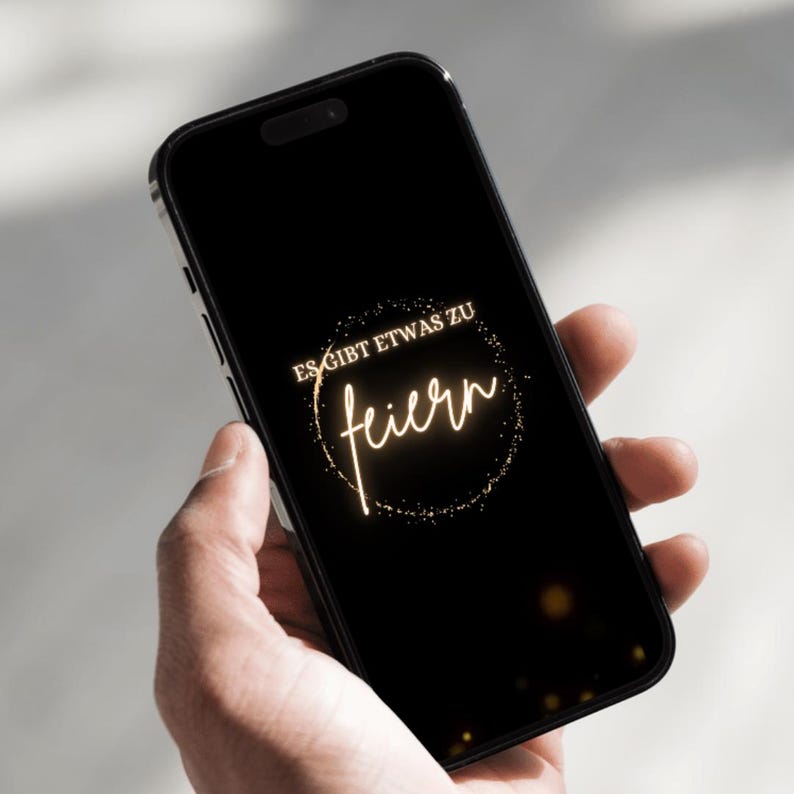 Puede incluir: Un smartphone negro muestra un mensaje de celebraci&oacute;n dorado sobre un fondo negro. El texto dice "ES GIBT ETWAS ZU feiern" en un dise&ntilde;o circular, sugiriendo una ocasi&oacute;n festiva.