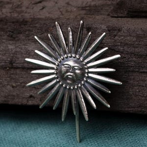 Peut inclure: Une broche en métal argenté représentant un visage de soleil central à l'expression sereine, entouré de nombreux rayons pointus rayonnants de longueurs variées. Le centre solaire circulaire est orné de petites perles sur son bord extérieur.