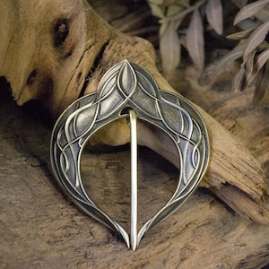 May include: A silver-toned metal brooch with an intricate Celtic knot design. The brooch is heart-shaped and has a pin closure.