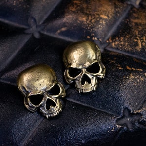 May include: Two gold-coloured skull-shaped charms on a black leather background.