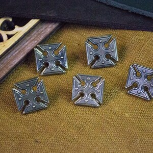 May include: Five silver-toned metal buttons with a cross design. Each button is square shaped with a cross in the centre and four smaller circles around the cross.