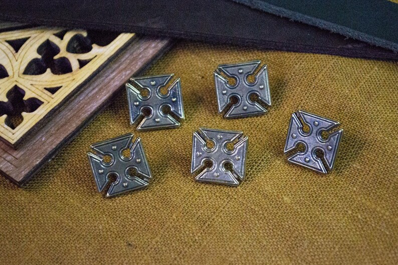 May include: Five silver-toned metal buttons with a cross design. Each button is square shaped with a cross in the centre and four smaller circles around the cross.