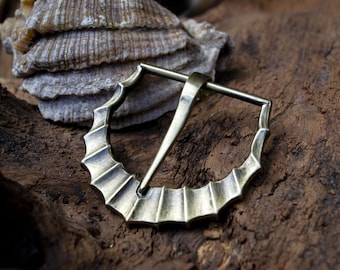 May include: A brass belt buckle with a decorative, scalloped edge. The buckle is designed to be used with a leather belt.
