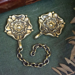 Pode incluir: Dois fechos de metal dourado em forma de rosa conectados por uma corrente. Os fechos têm um design detalhado e são perfeitos para adicionar um toque de elegância a qualquer projeto.