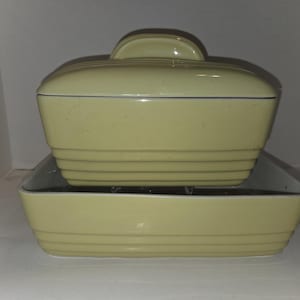 May include: A pale yellow ceramic casserole dish with a matching lid and a rectangular baking dish. The casserole dish has a handle on top and horizontal ridges. The baking dish is rectangular with horizontal ridges.