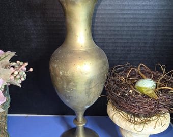 May include: A vintage brass vase with a ruffled rim. The vase has a bulbous body and a flared base. The vase is approximately 10 inches tall. A decorative bird's nest with an egg sits nearby.
