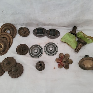 May include: A collection of antique hardware components, including decorative rosettes, drawer pulls, and knobs. The pieces are made of metal and feature various designs, including floral and geometric patterns. Some components have a distressed finish.
