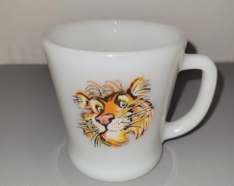 May include: A white milk glass mug featuring a colorful illustration of a tiger face on the front. The mug has a smooth, tapered body with a curved handle on the right side. The tiger graphic displays orange, black, and white fur details.
