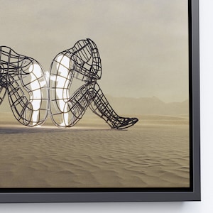 May include: A black metal sculpture of two figures sitting back to back in a desert landscape. The figures are made of a wire mesh and are partially filled with light.