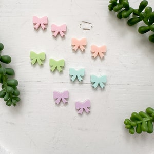 May include: Assortment of pastel-colored plastic bows. The bows are in shades of pink, green, and blue.
