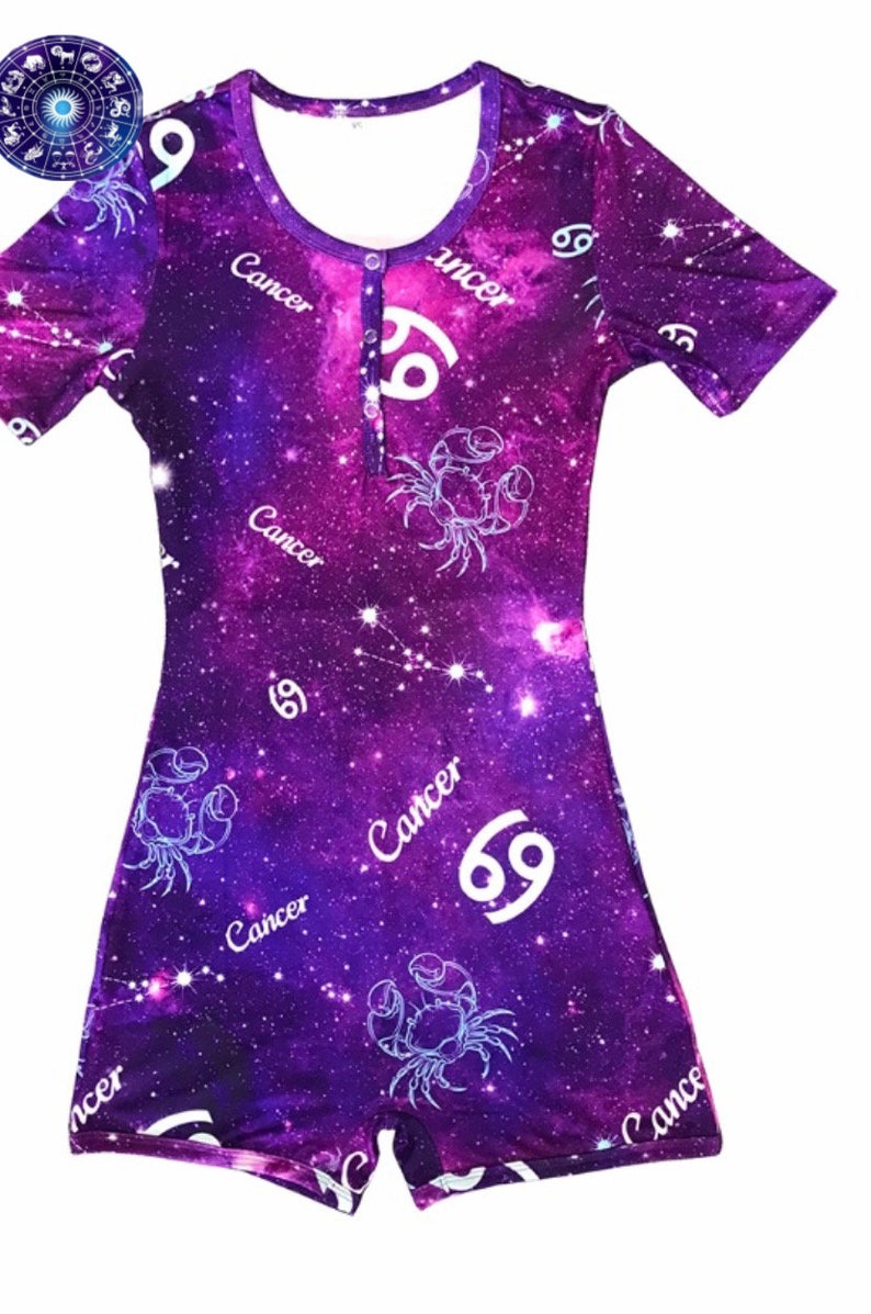 May include: Purple onesie with a galaxy print featuring the Cancer zodiac sign and the word "Cancer" repeated throughout the design.