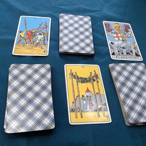 May include: A tarot card spread with illustrated cards and text, arranged on a dark teal surface. The cards depict figures, symbols, and the word "JUDGEMENT". The card backs have a blue and white plaid design. The image suggests divination or fortune-telling.
