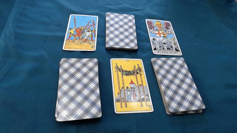 May include: A tarot card spread with illustrated cards and text, arranged on a dark teal surface. The cards depict figures, symbols, and the word "JUDGEMENT". The card backs have a blue and white plaid design. The image suggests divination or fortune-telling.