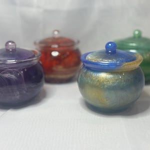 May include: Four small glass jars with lids. The jars are filled with colorful resin and have a variety of colors, including purple, blue, green, and red.