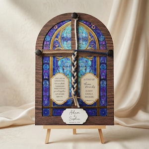 May include: Wooden framed stained glass art piece with a braided cord. The artwork features a blue and purple stained glass design with text that reads "A cord of three strands is not easily broken." A small easel supports the frame.