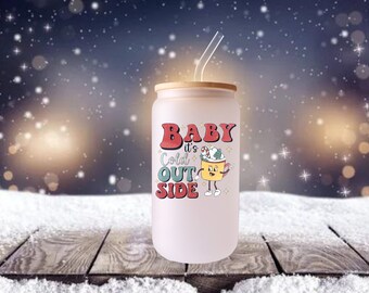 May include: A frosted glass tumbler with a bamboo lid and a clear straw. The tumbler features the phrase "BABY it's COLD OUT SIDE" in red, teal, and white lettering, along with a cartoon coffee cup graphic. The design has a retro aesthetic.