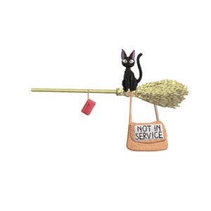 May include: An embroidered design featuring a black cat perched on a broom. The broom has a straw head and a wooden handle. A small red package and a tan bag with "NOT IN SERVICE" are hanging from the broom.