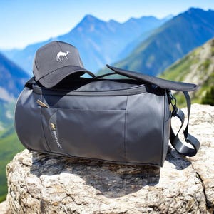May include: Black duffel bag with a black and white camel logo and a black baseball cap with a white camel logo on top of it.