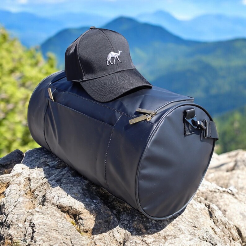 May include: Black duffel bag with a black baseball cap on top. The cap has a white camel embroidered on the front.