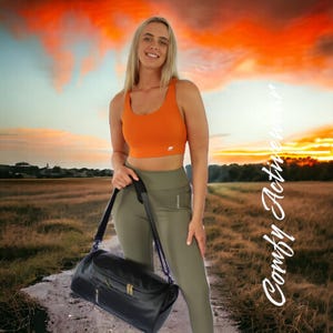 May include: A woman wearing an orange sports bra and olive green leggings is holding a black duffel bag. The background is a sunset sky with clouds.