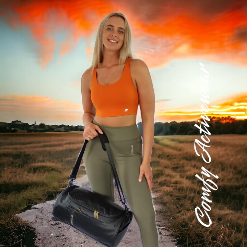 May include: A woman wearing an orange sports bra and olive green leggings is holding a black duffel bag. The background is a sunset sky with clouds.