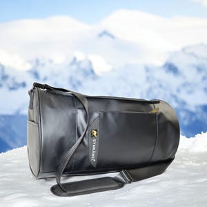 May include: Black duffel bag with a black shoulder strap and a gold logo that says "GYMK&Auml;MEL".