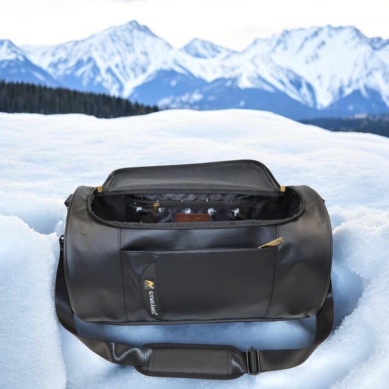 May include: Black leather duffel bag with a gold zipper and a small pocket on the front. The bag has a shoulder strap and is open, revealing a black and white patterned lining.