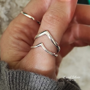 May include: Two silver chevron rings stacked on a finger. The rings are simple and modern in design.