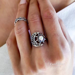 Puede incluir: Se muestran dos anillos de plata, uno con un diseño de luna creciente y sol, y otro con un patrón trenzado. Los anillos se muestran en una mano.
