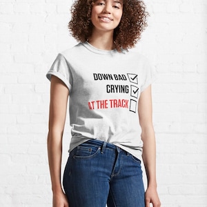 May include: A white t-shirt with a black checklist that says "Down Bad", "Crying", and "At The Track" with checkmarks next to each item.