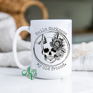 May include: White ceramic mug featuring a black and white graphic of a skull with flowers and a butterfly. The text "Hello darkness my old friend." is printed on the mug.