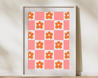Op de afbeelding: Een ingelijste kunstdruk met een retro bloemenpatroon. Het ontwerp toont oranje bloemen op een roze en witte geruite achtergrond. Het kunstwerk wordt gepresenteerd in een witte lijst, wat een schoon, modern contrast biedt met het bloemmotief.