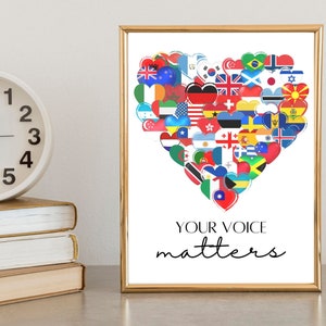 May include: A framed print with a gold border displays a heart made of international flags. The text "YOUR VOICE matters" is written in black script below. A white clock and stacked books are in the foreground, adding to the composition.