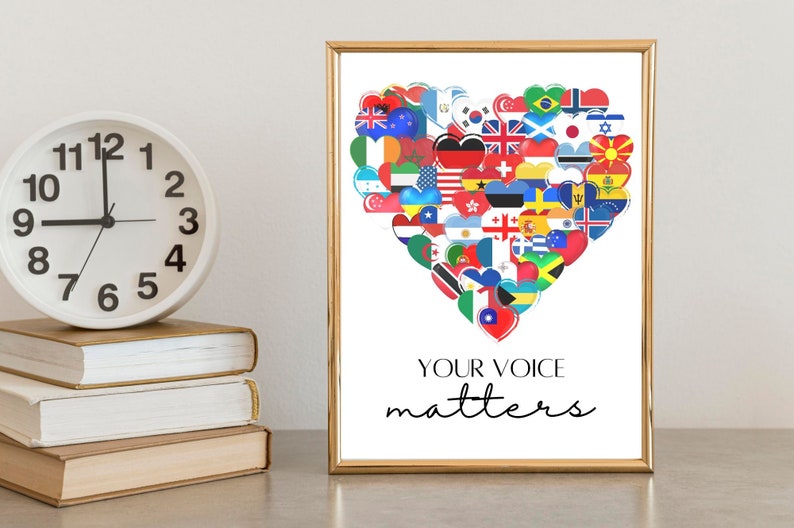 May include: A framed print with a gold border displays a heart made of international flags. The text "YOUR VOICE matters" is written in black script below. A white clock and stacked books are in the foreground, adding to the composition.