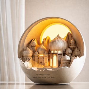 May include: An illuminated sculpture depicting a Middle Eastern city with domes and mountains, housed within a cracked eggshell-shaped frame. The warm yellow light creates a sunset effect. The text reads: "Tenderness is the eternal light in the dark world." The sculpture is a decorative item.