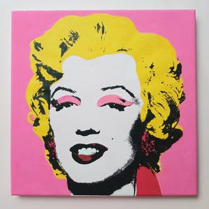 Puede incluir: Una pintura pop art de Marilyn Monroe con fondo rosa, cabello amarillo, ojos negros y labios rojos.