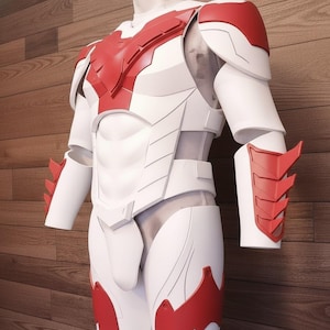 Puede incluir: Un traje de superhéroe blanco y rojo exhibido en un maniquí. El traje presenta una placa pectoral, hombreras, protectores de brazos y armadura para las piernas. El diseño incorpora detalles rojos sobre una base blanca, con una estética futurista.