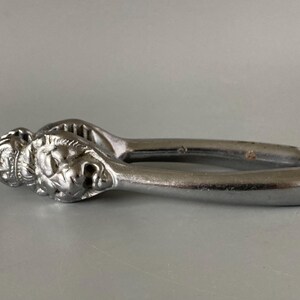 May include: A silver metal nutcracker featuring a lion's head design. The nutcracker has a lever mechanism and is designed for cracking nuts. The lion's head is intricately detailed with a mane and facial features.
