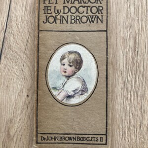 May include: A rectangular tan-coloured book titled Pet Marjorie by Doctor John Brown. The cover features a central oval illustration of a child with light brown hair wearing a white shirt. The bottom text reads Dr. John Brown Booklets II.