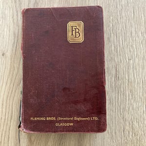 May include: A vintage maroon hardcover book with a gold embossed logo featuring the letters FB inside a rectangular border. The text Fleming Bros. (Structural Engineers) Ltd. Glasgow is printed in gold at the bottom of the front cover.