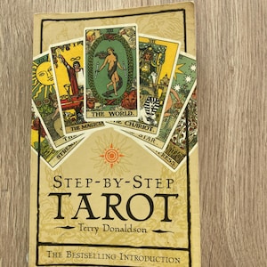 May include: A well-worn copy of "Step-by-Step Tarot" by Terry Donaldson. The cover displays a collection of tarot card images and the title. The book is set against a wooden background, with the text "The Bestselling Introduction".