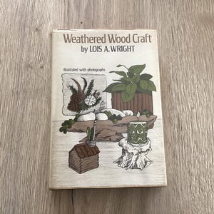 May include: A book titled "Weathered Wood Craft" by Lois A. Wright, illustrated with photographs. The cover features a drawing of a wooden cabin, a potted plant, and a candle.