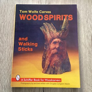 May include: A book titled "Woodspirits and Walking Sticks" by Tom Wolfe Carves. The cover shows a carved wooden face with a long beard. The book is a Schiffer Book for Woodcarvers.