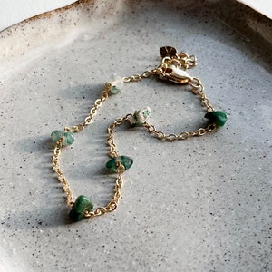 May include: A gold chain bracelet with green gemstone accents. The bracelet has a lobster clasp closure.