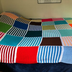 May include: A colorful knitted patchwork blanket with squares of different colors and patterns, including stripes, solid colors, and a mix of both.