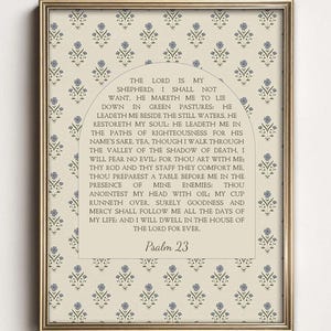 May include: A framed wall art print featuring a cream background with a repeating pattern of small blue floral sprigs. Centered is an arched beige panel containing the full text of Psalm 23 in black serif font, ending with the title Psalm 23.