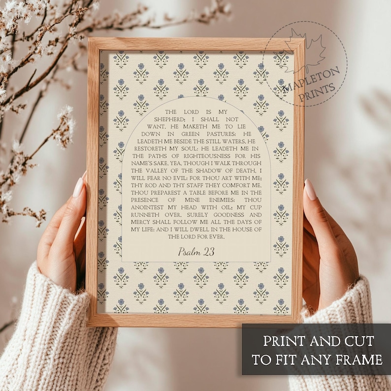 May include: A framed print featuring Psalm 23 text centered within an arched design. The background displays a repeating pattern of small blue floral motifs on a cream-colored surface. The frame is made of light-toned wood with a simple profile.