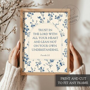 May include: A framed print with the text "Trust in the Lord with all your heart and lean not on your own understanding" from Proverbs 3:5. The print has a floral design with blue flowers on a cream background. The frame is a light brown color.