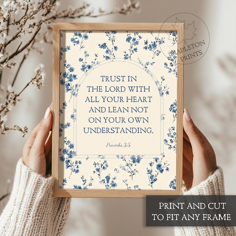 May include: A framed print with the text "Trust in the Lord with all your heart and lean not on your own understanding" from Proverbs 3:5. The print has a floral design with blue flowers on a cream background. The frame is a light brown color.