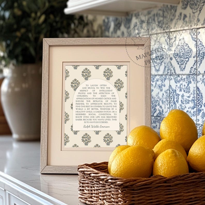May include: A framed print with a white background and a gray floral pattern. The print features a quote by Ralph Waldo Emerson about laughter, respect, and the importance of leaving the world a better place. The print is displayed on a countertop with lemons in a wicker basket.